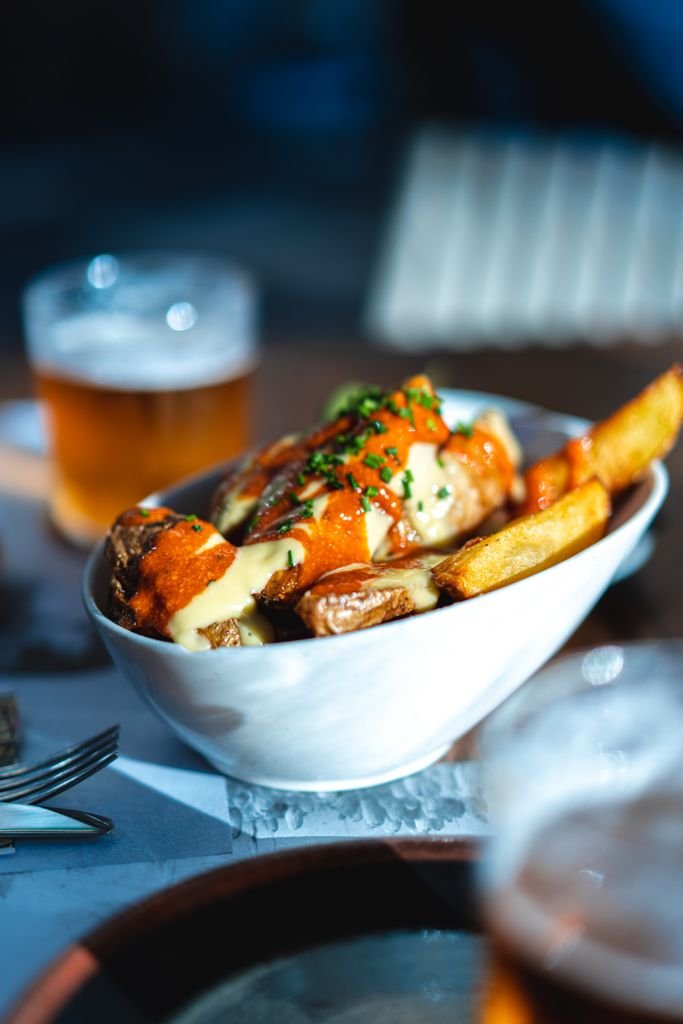 A delicious bowl of poutine topped with cheese and sauce, accompanied by a glass of beer.