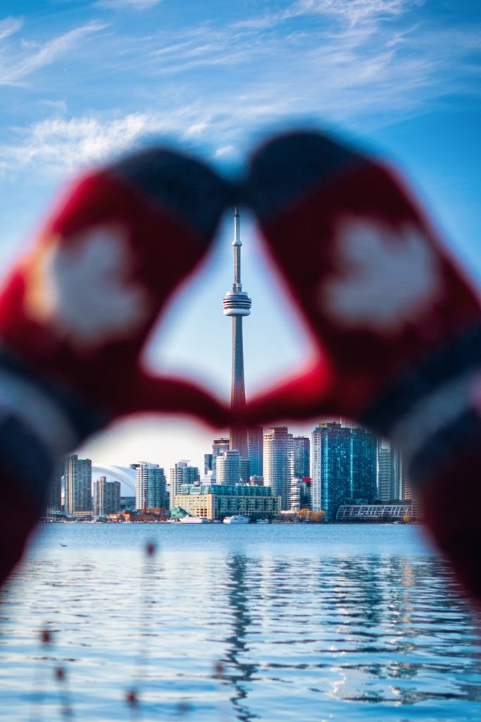 Creative view of Toronto skyline with CN Tower framed by hands in mittens forming a heart.